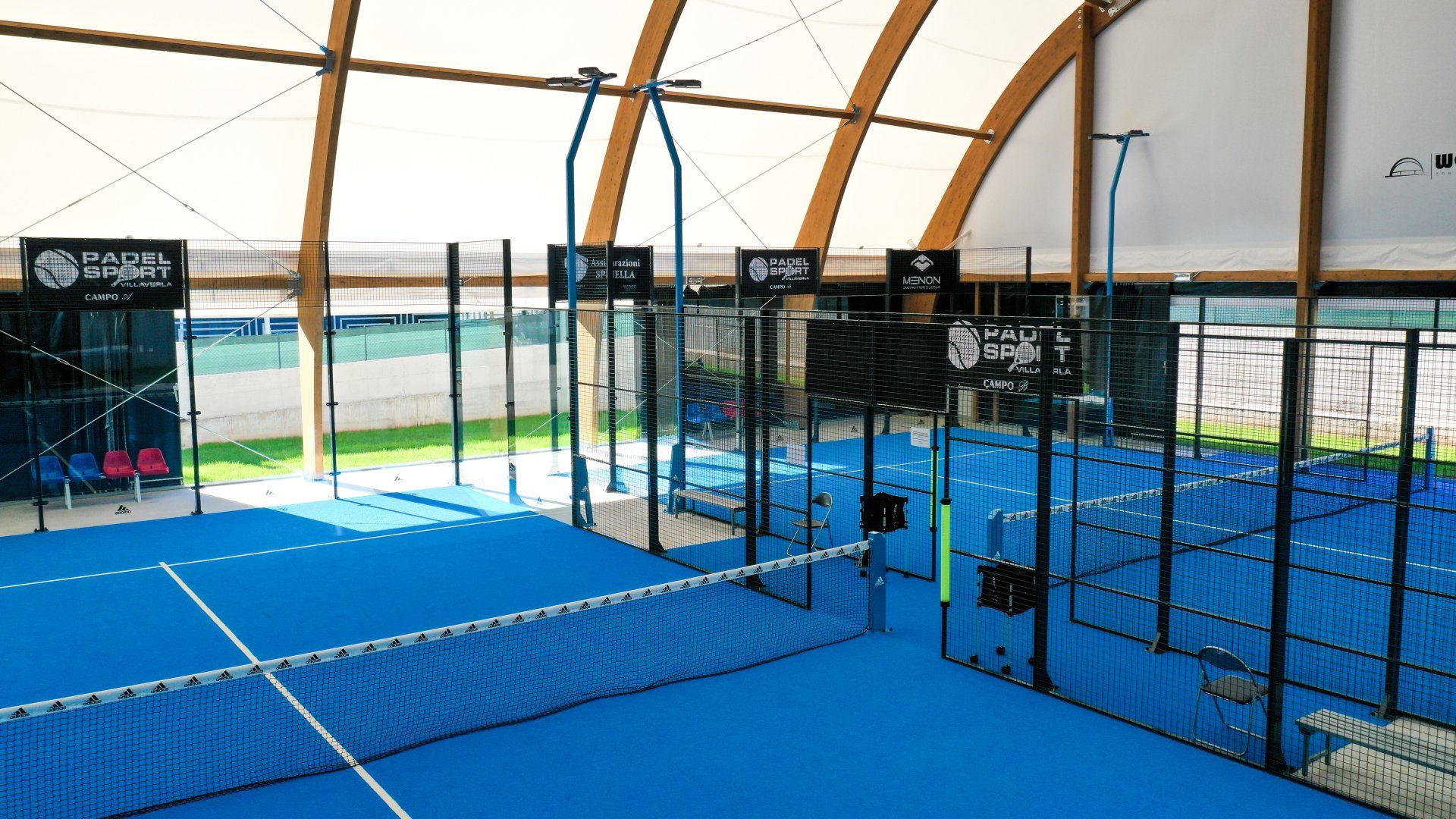 Campi da padel indoor con superfici e reti blu, visti da un'angolazione elevata.