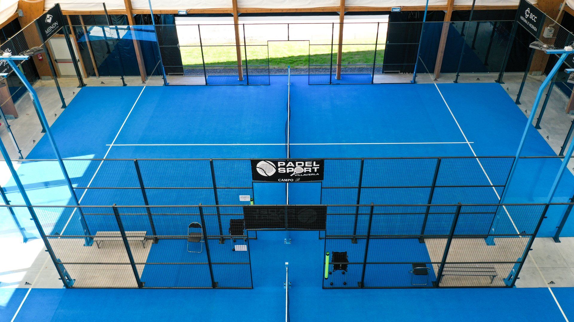 Campo da padel blu al coperto, con una panchina nera e un logo al centro.