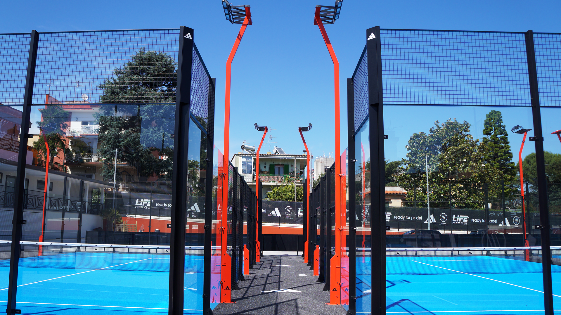 Campo da padel con superficie blu e strutture di supporto arancioni sotto un cielo limpido.