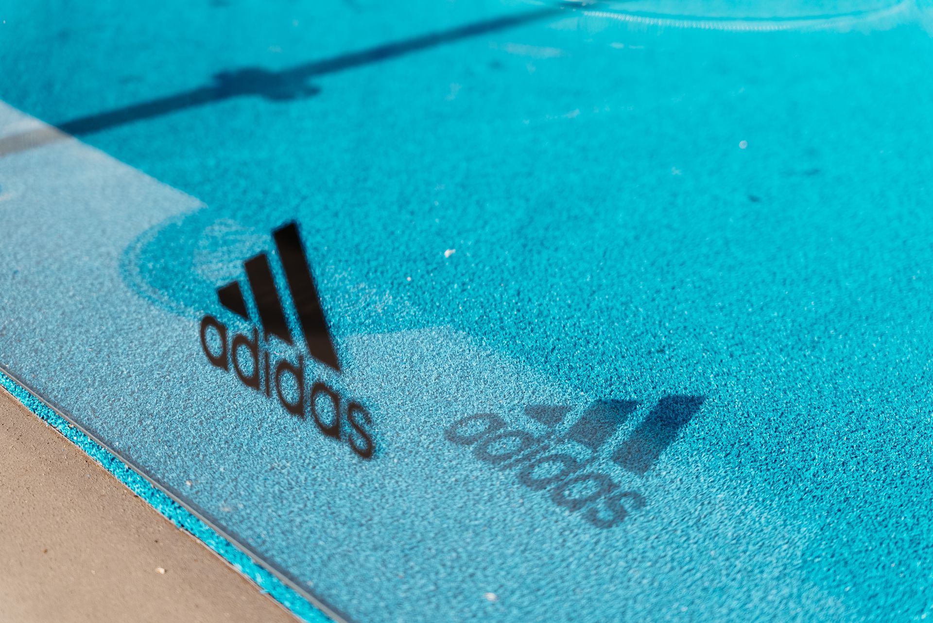 Logo Adidas su una superficie blu, con un'ombra del logo visibile.