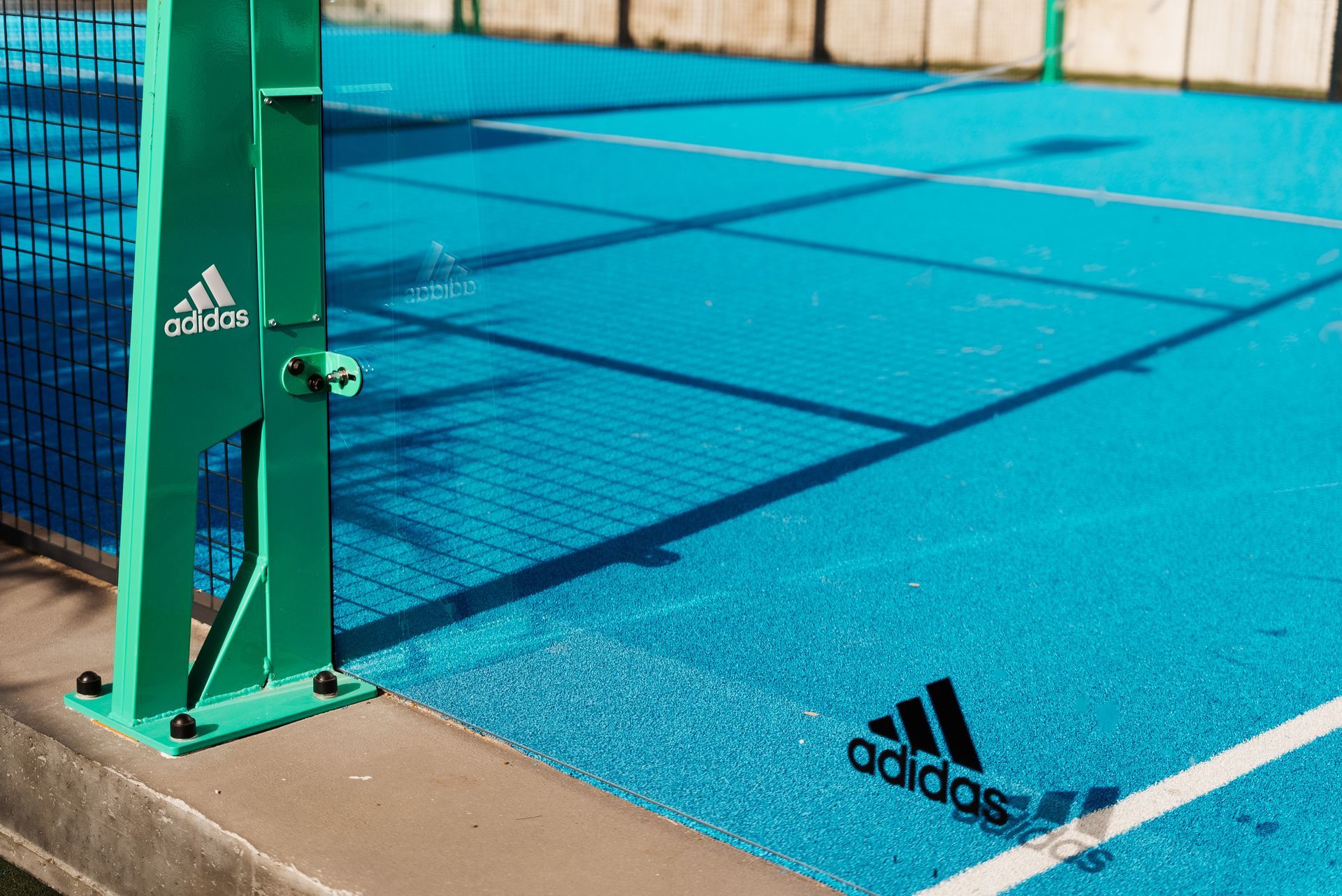 Campo da padel verde e blu con marchio Adidas.
