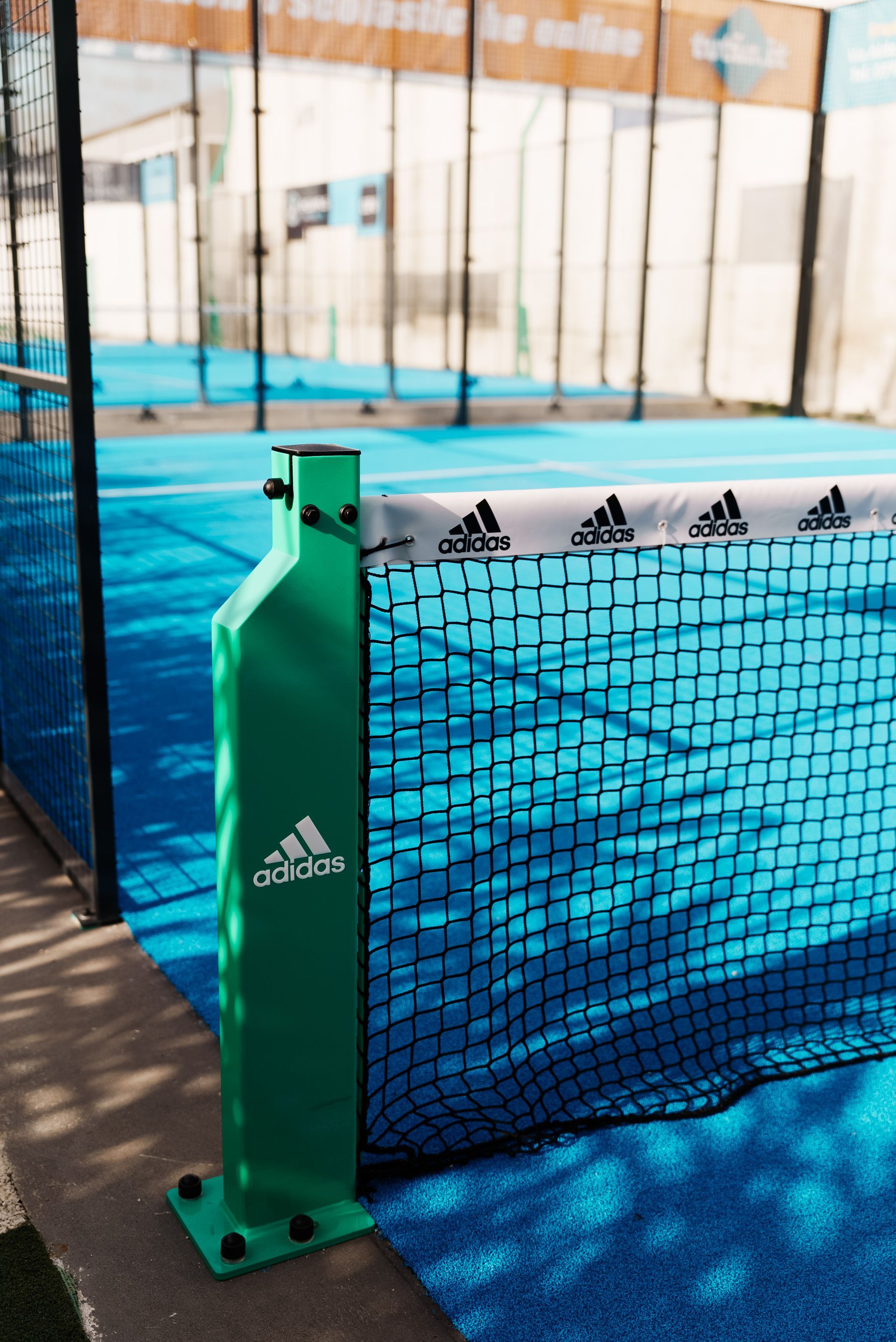 Palo verde Adidas su un campo da padel blu con rete Adidas.