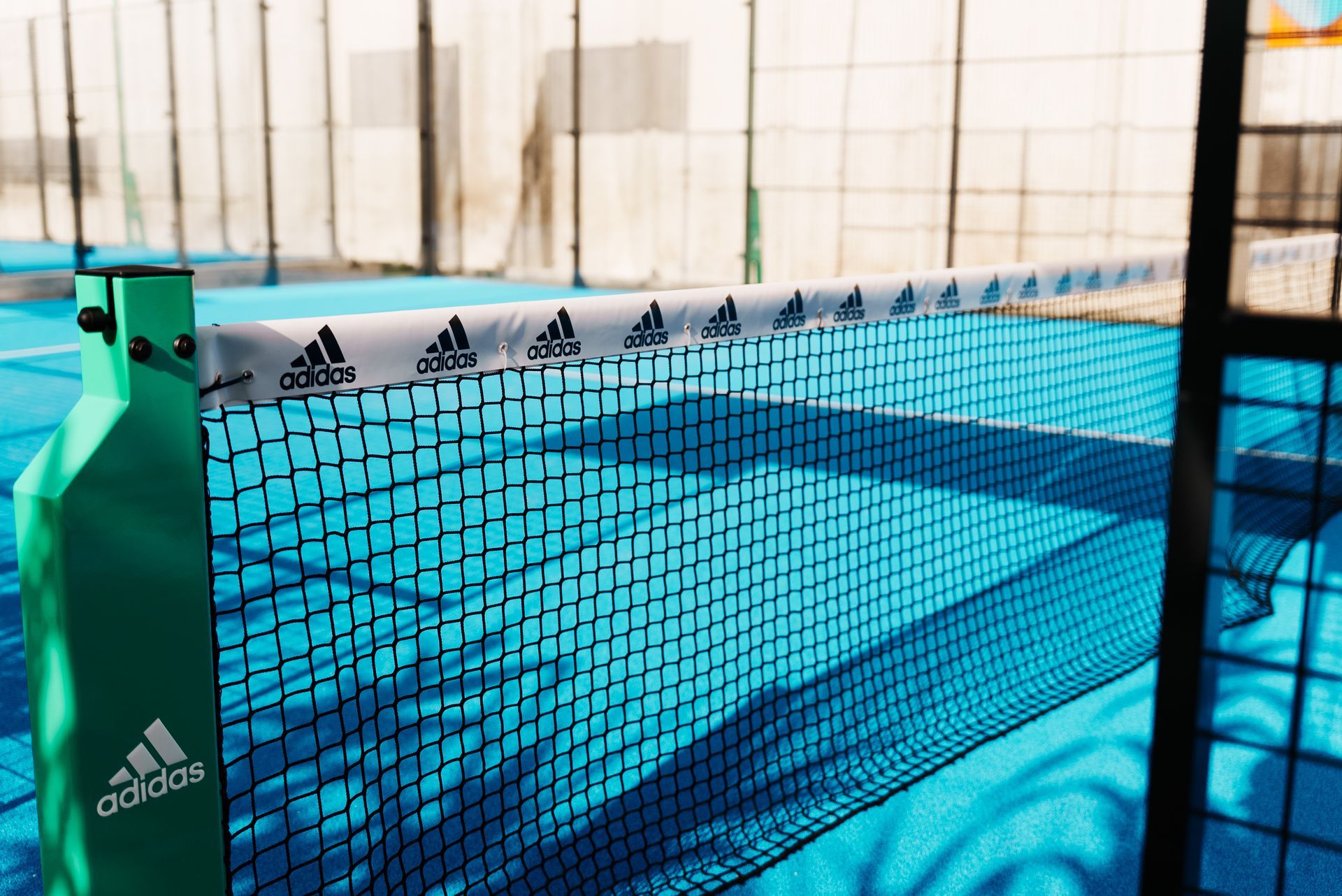 Rete da padel tennis con logo Adidas su un campo turchese.