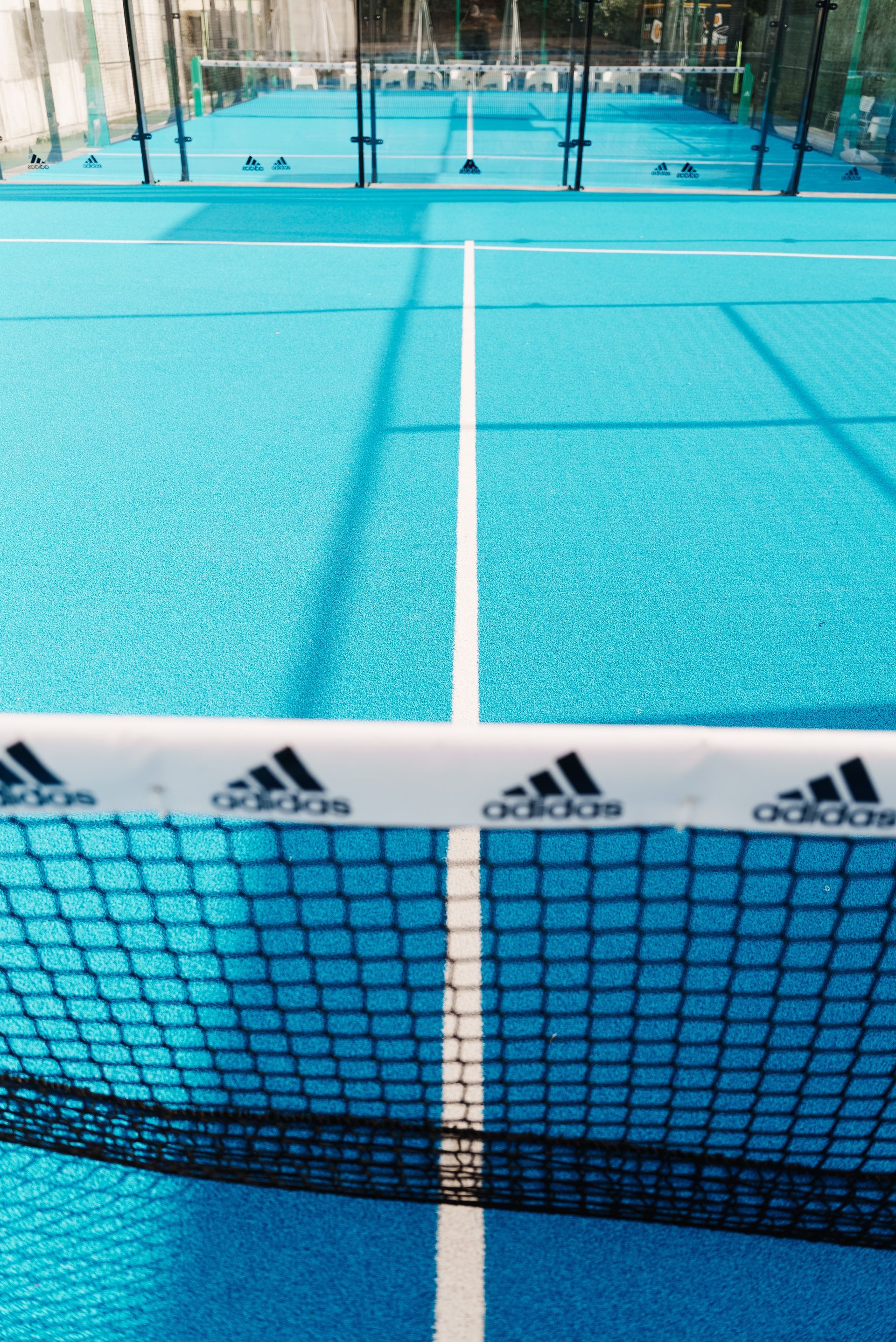 Campo da paddle tennis blu con rete e logo Adidas.
