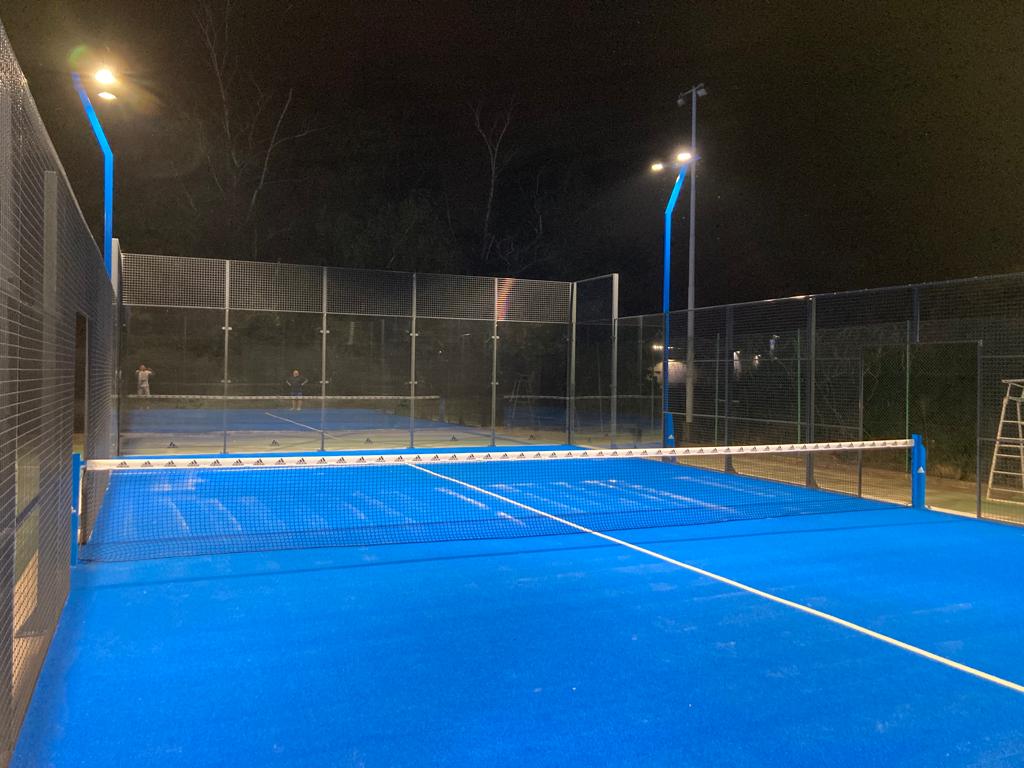 Campo da padel illuminato di notte, reti e recinzioni visibili.