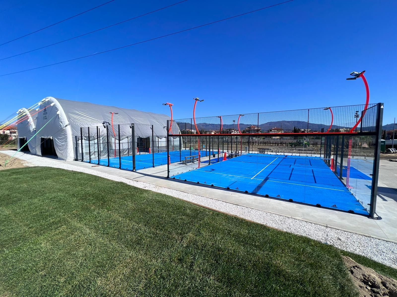 Campi da padel con superfici blu e una recinzione bianca ad arco, accanto a un sentiero in erba 