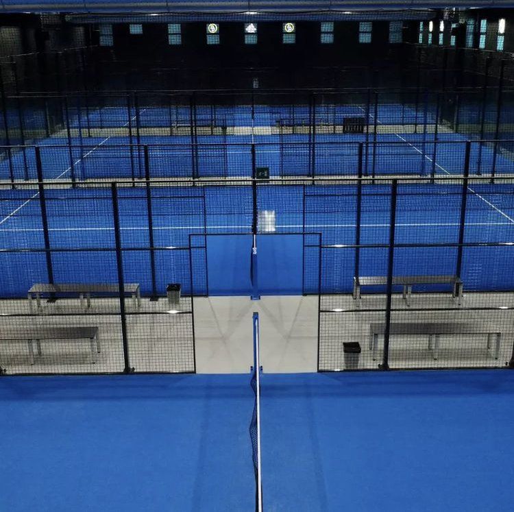 Campi da padel blu al coperto con reti e recinzioni circostanti, vuoti.