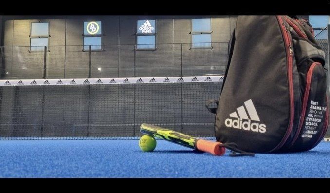 Borsa sportiva Adidas e racchetta con una palla su un campo blu.