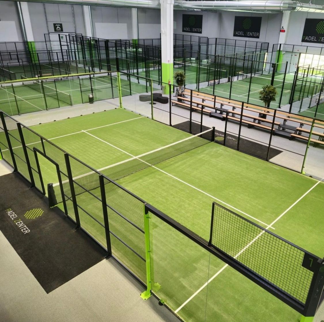 Campo da padel indoor con erba verde, recinzione nera e vista dall'alto.