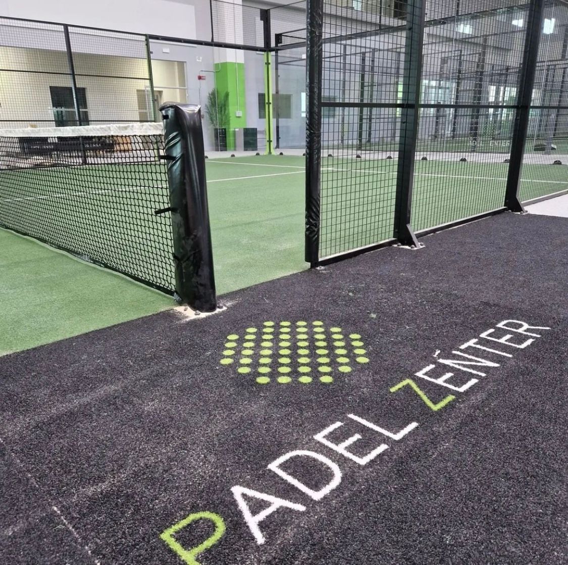 Campo da padel al coperto con pavimentazione nera, campo da padel verde e logo 