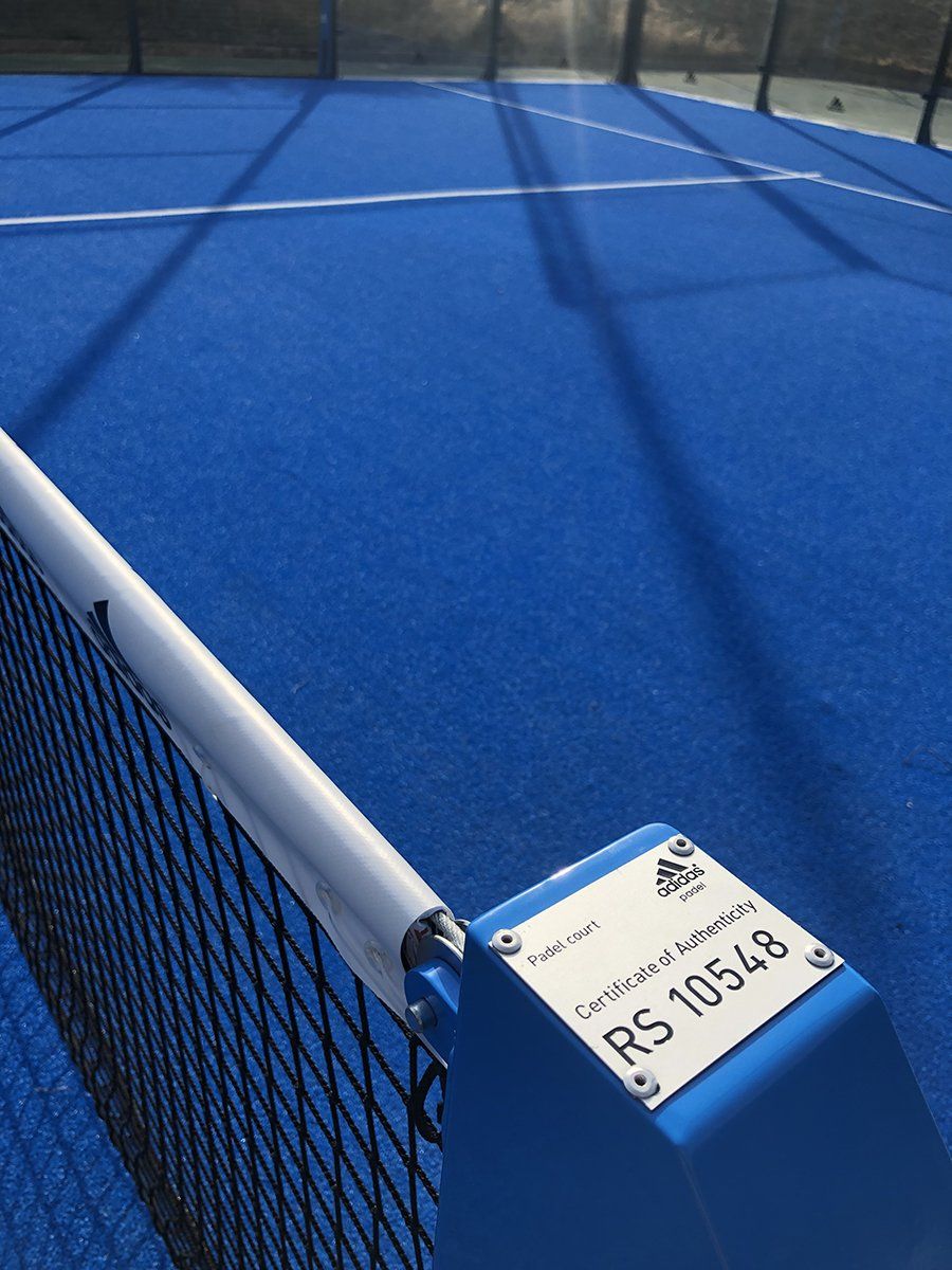 Campo da padel blu con rete, linee bianche e un'etichetta di certificazione sul palo della rete.