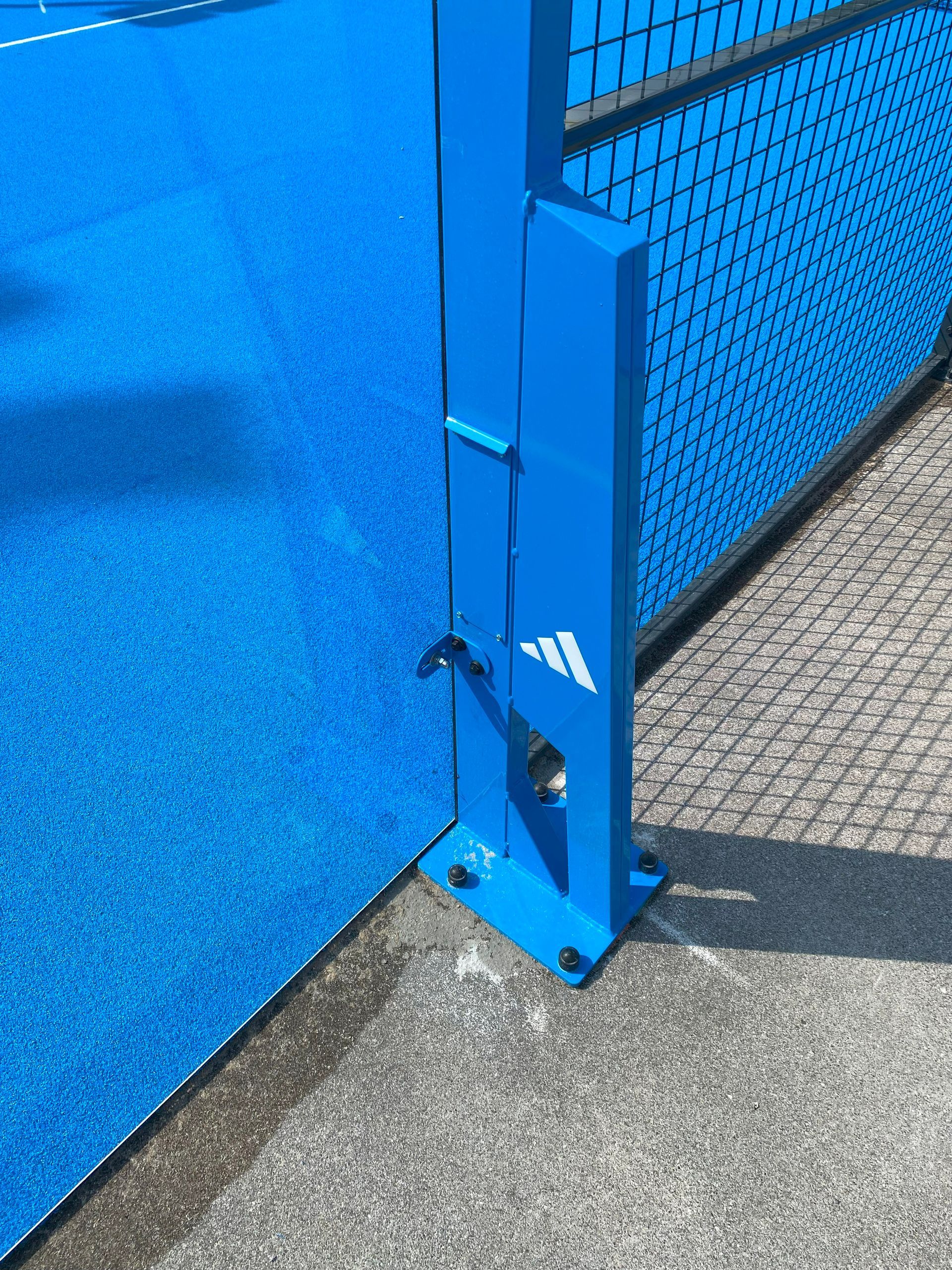 Palo di metallo blu con logo Adidas, parte di una rete sportiva su un campo blu.