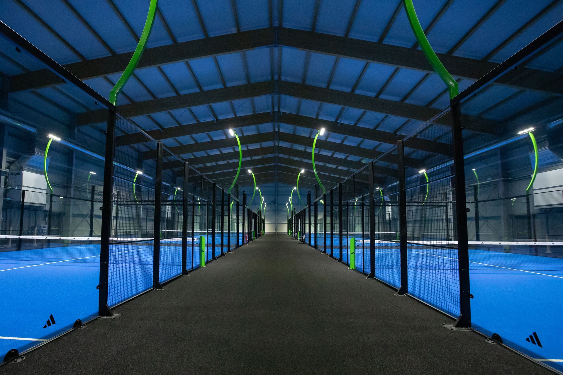 Campo da padel blu al coperto con una fila di campi. Illuminazione dall'alto. Rete nera.