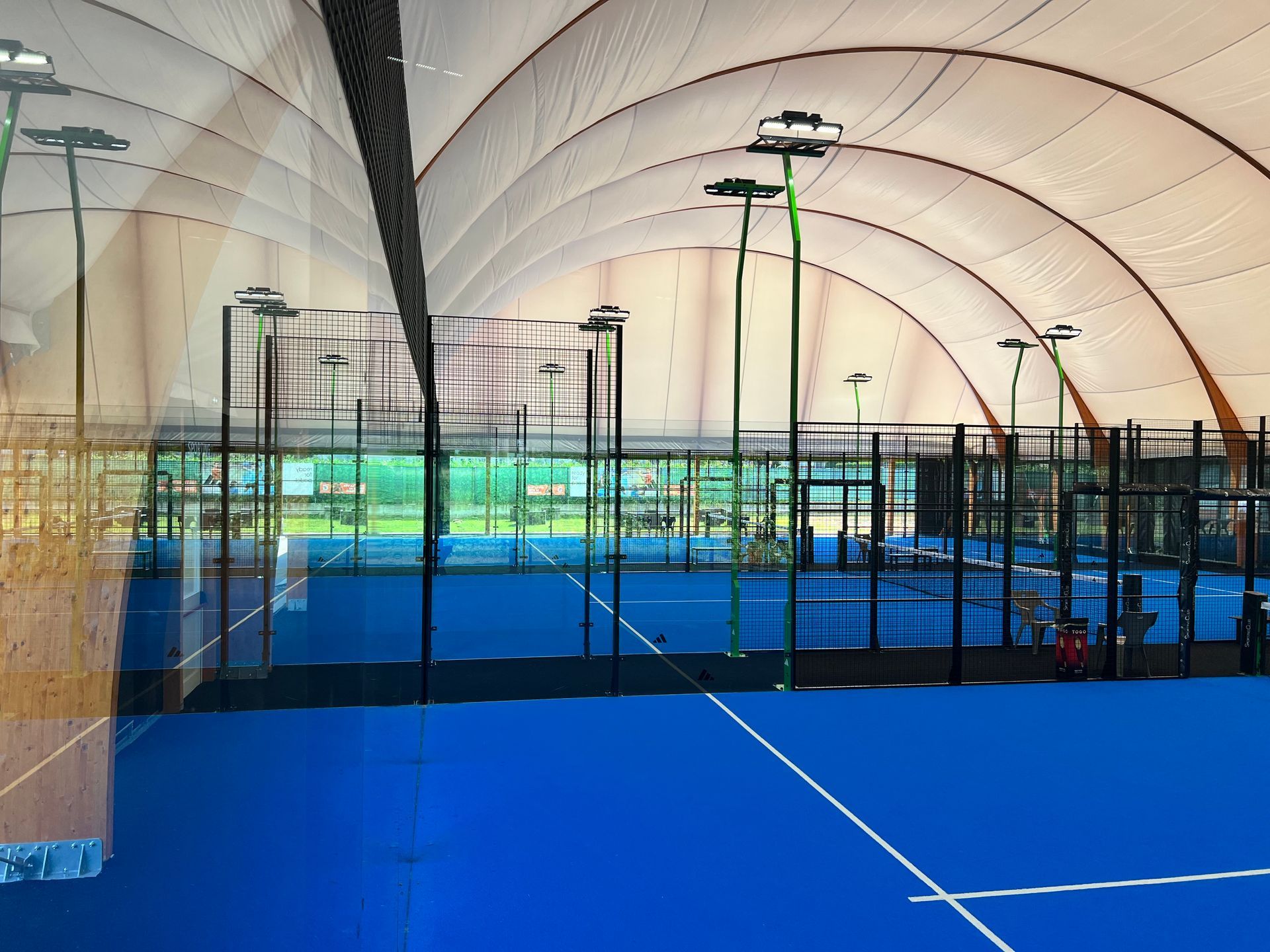 Campo da padel indoor con superficie blu e alti pali della luce verdi.