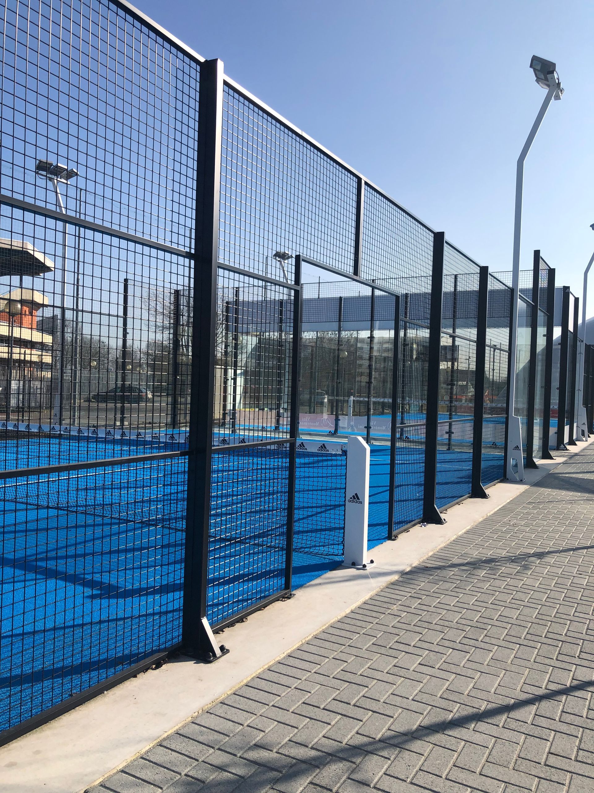 Campo da padel blu con rete nera e passerella a lato.