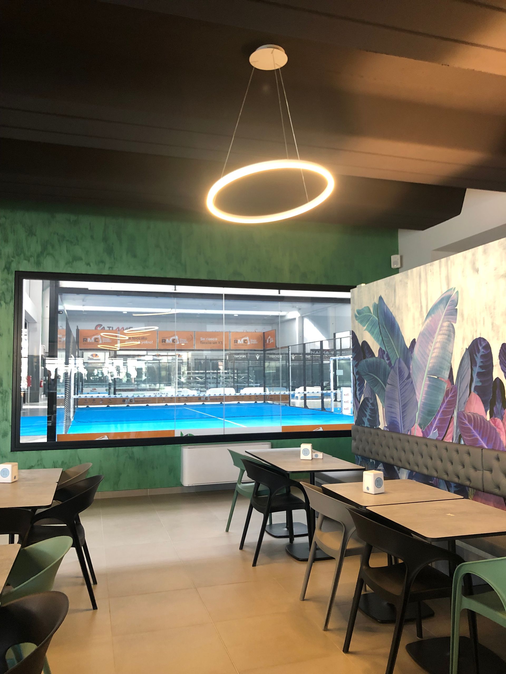 Interno del ristorante con vista sulla piscina, tavoli, sedie, pareti verdi e un lampadario circolare.