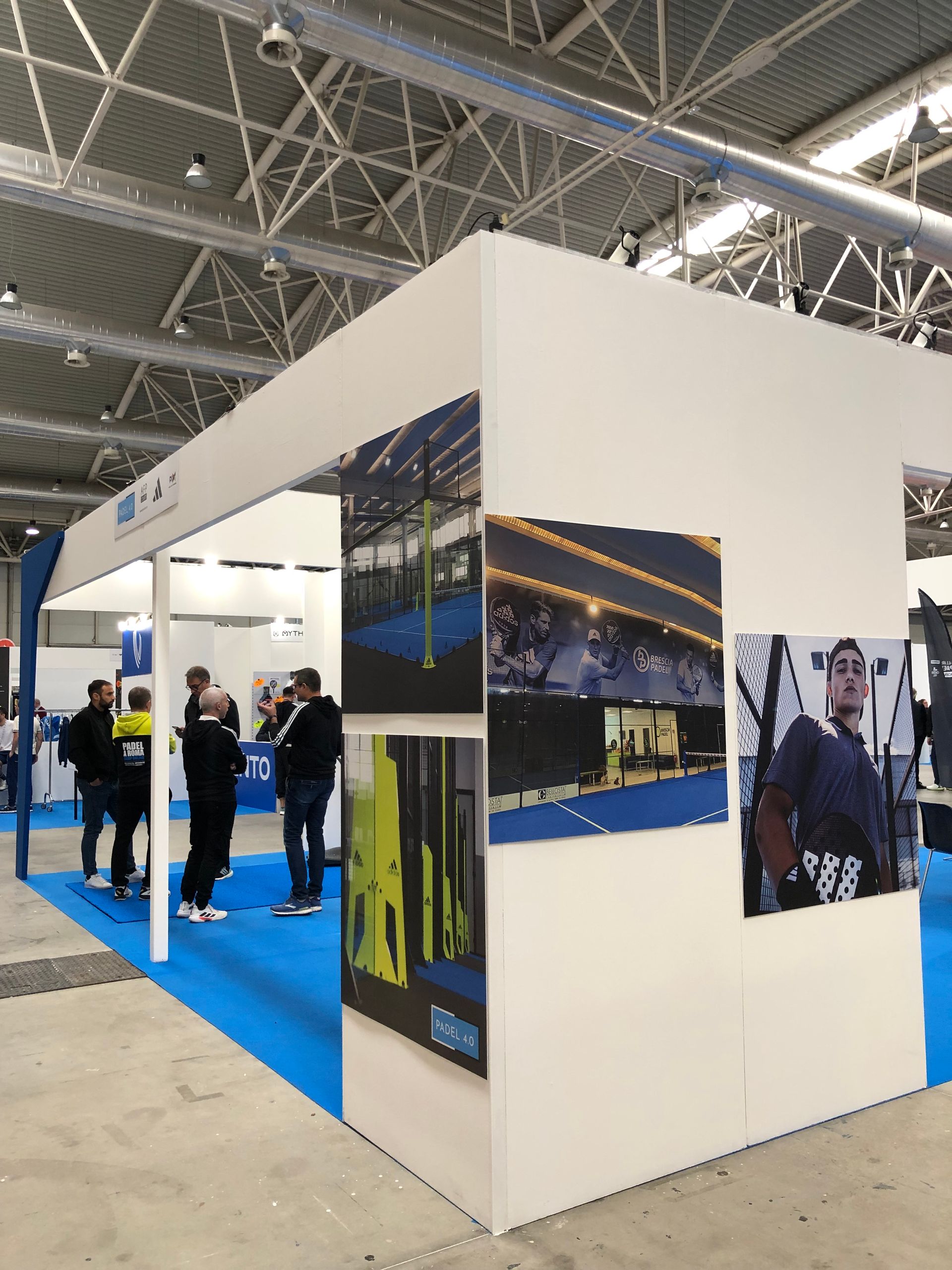 Stand con foto alle pareti, persone vicino all'ingresso. Pareti bianche, moquette blu.