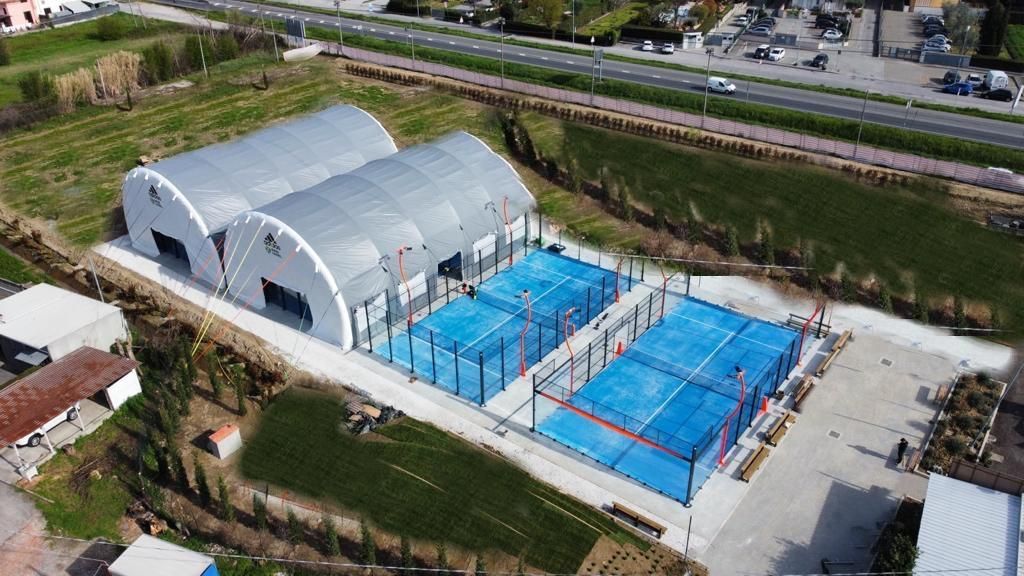 Vista aerea di un complesso di campi da padel con due campi coperti e quattro campi all'aperto, tutti blu.