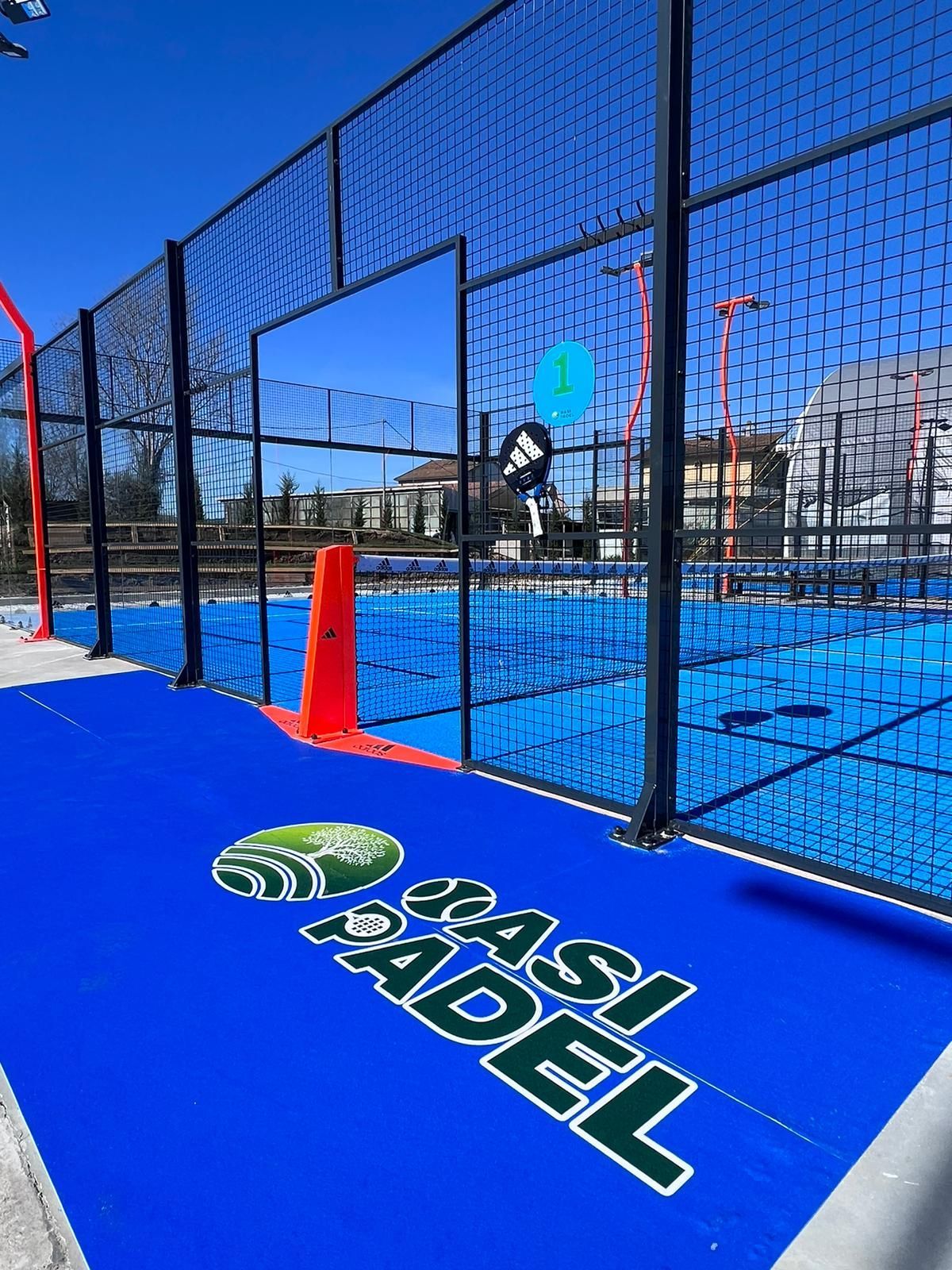 Campo da padel blu con rete nera, logo "Rasi Padel" e cono arancione.