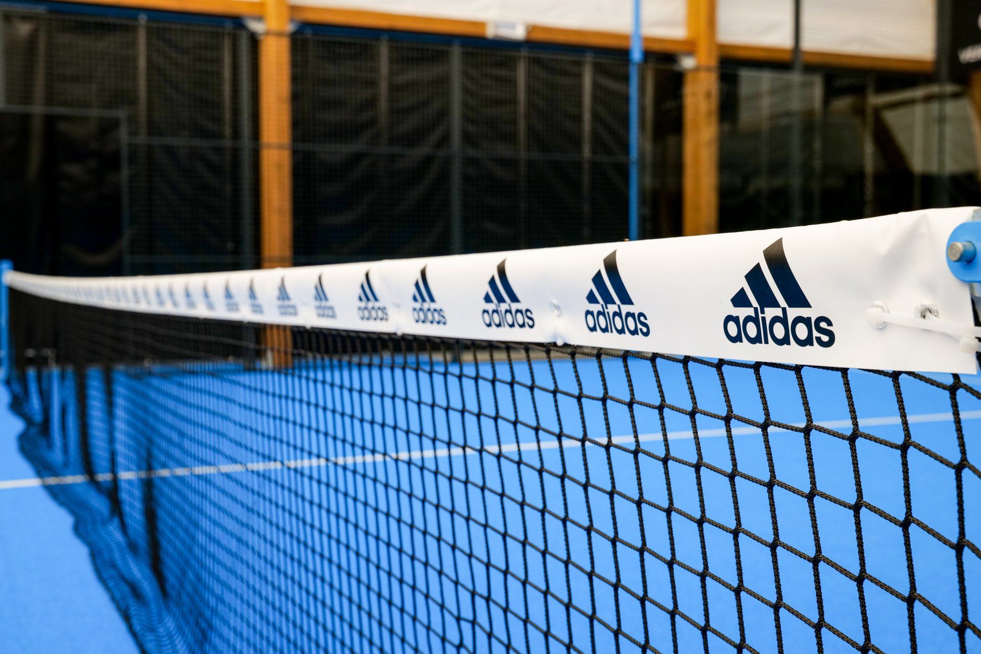 Logo Adidas su una rete da tennis in un campo coperto blu.