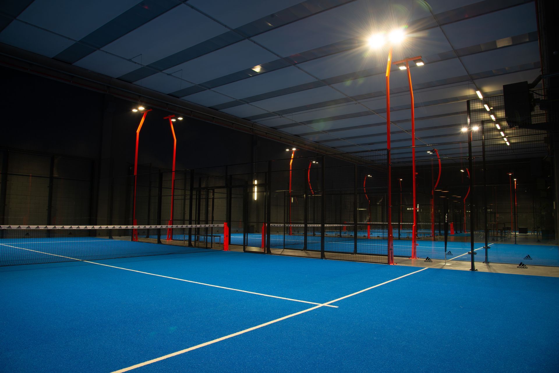 Campo da padel blu al coperto con supporti rossi e neri. Illuminazione dall'alto.