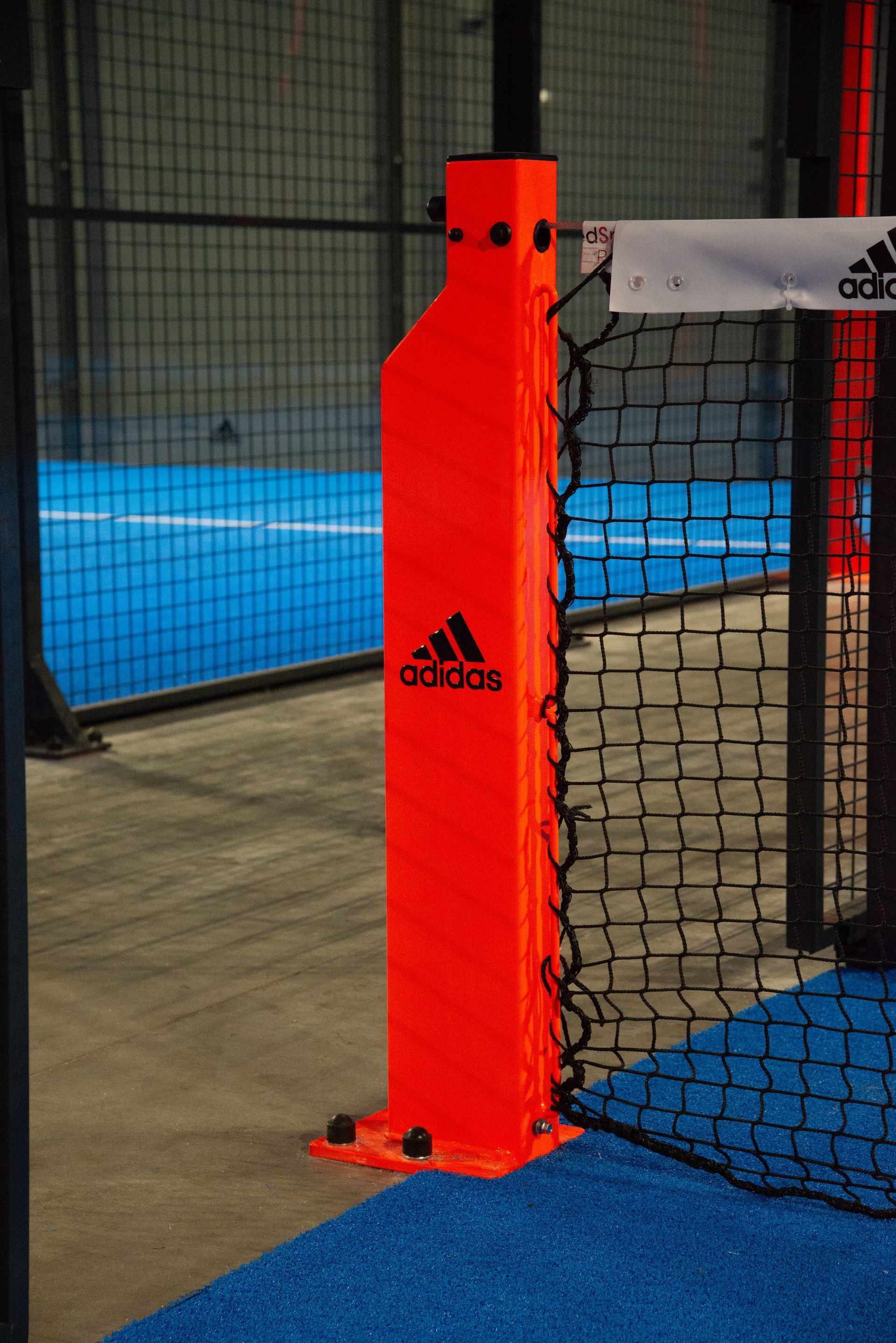 Palo arancione con il marchio Adidas su un campo da padel blu e grigio.