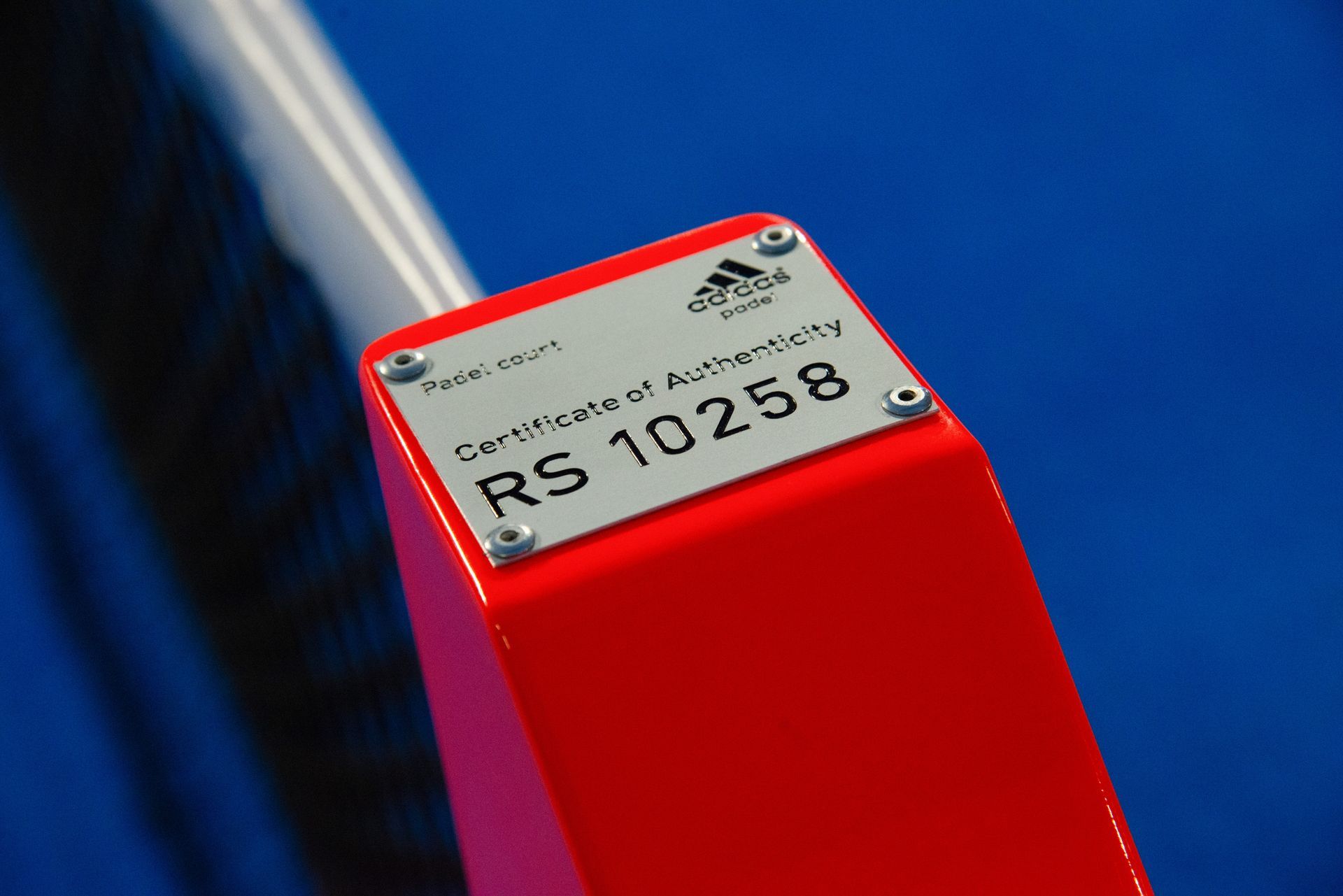 Primo piano Adidas rossa con una targhetta argentata del Certificato di autenticità che riporta la dicitura 