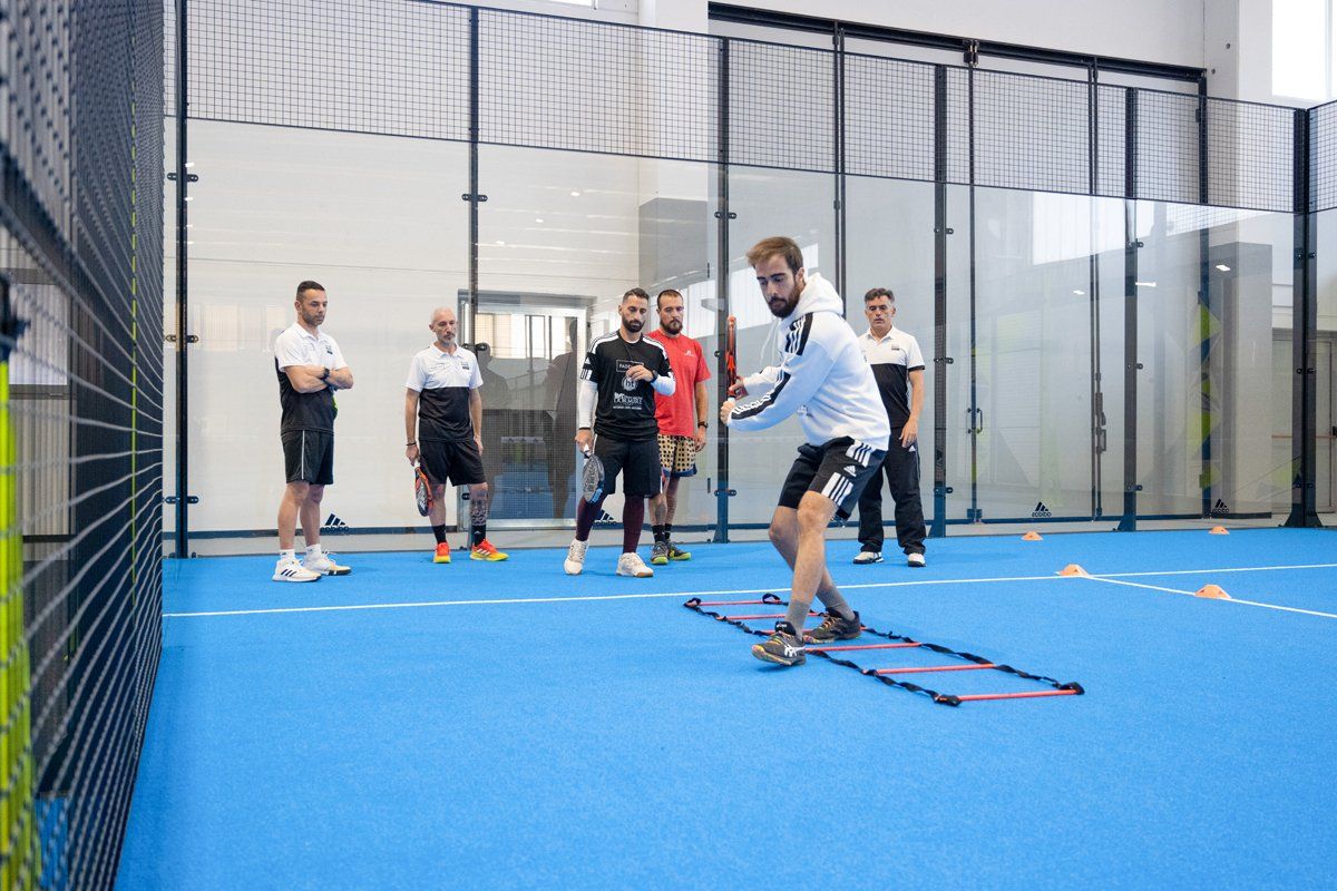 Un uomo pratica sport e brandisce una racchetta sul campo blu, osservato da diversi uomini.