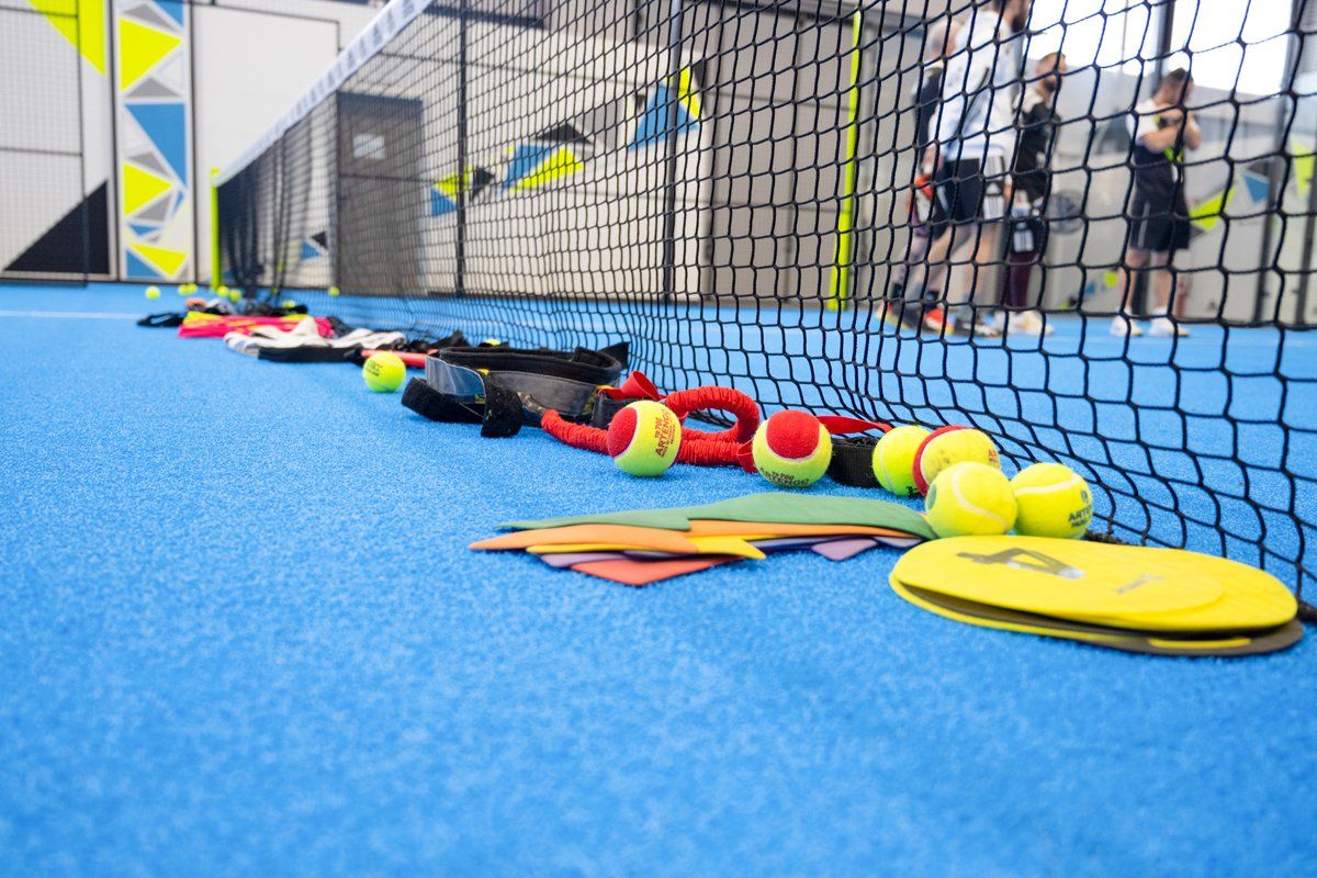 Campo da padel blu con attrezzatura e giocatori dietro la rete.