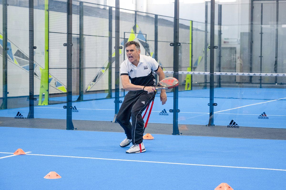 Uomo che gioca a padel sul campo blu, con la racchetta in mano, mentre si esercita con i coni arancioni