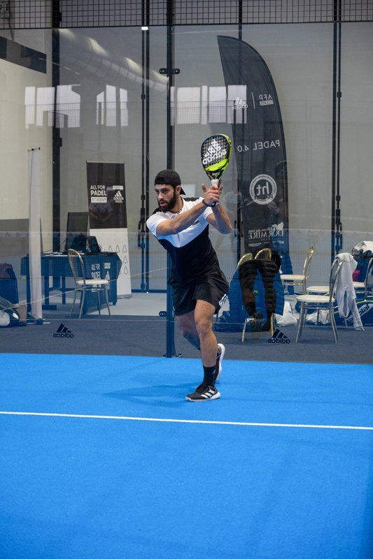 Uomo in abbigliamento sportivo che gioca a padel su un campo blu, con la racchetta alzata.