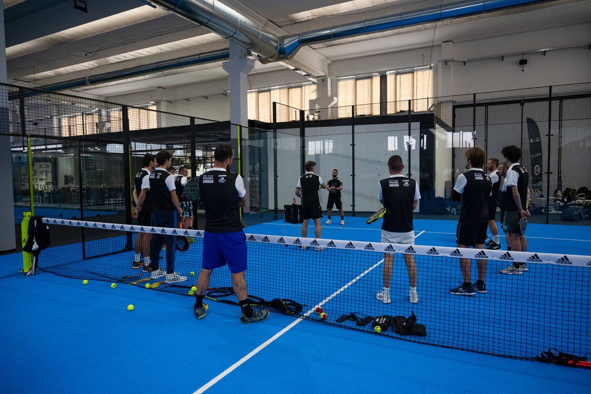 Gruppo di persone che giocano a padel tennis su un campo blu, con rete e palline.