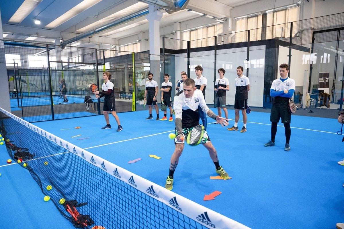 Persone che giocano a padel tennis su un campo blu, sotto gli occhi degli spettatori.