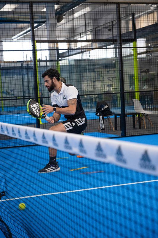 Uomo che gioca a padel tennis, abbigliamento sportivo. Rete, campo blu. Ambiente al coperto.
