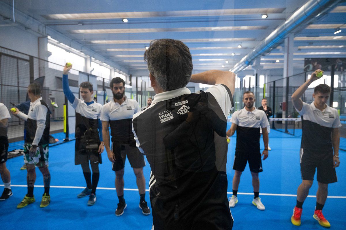 Istruttore che insegna a padel tennis; i giocatori tengono le palline, campo blu.