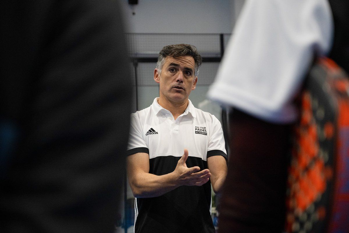 Uomo in camicia bianca e nera che gesticola, parlando a un gruppo; ambiente interno.