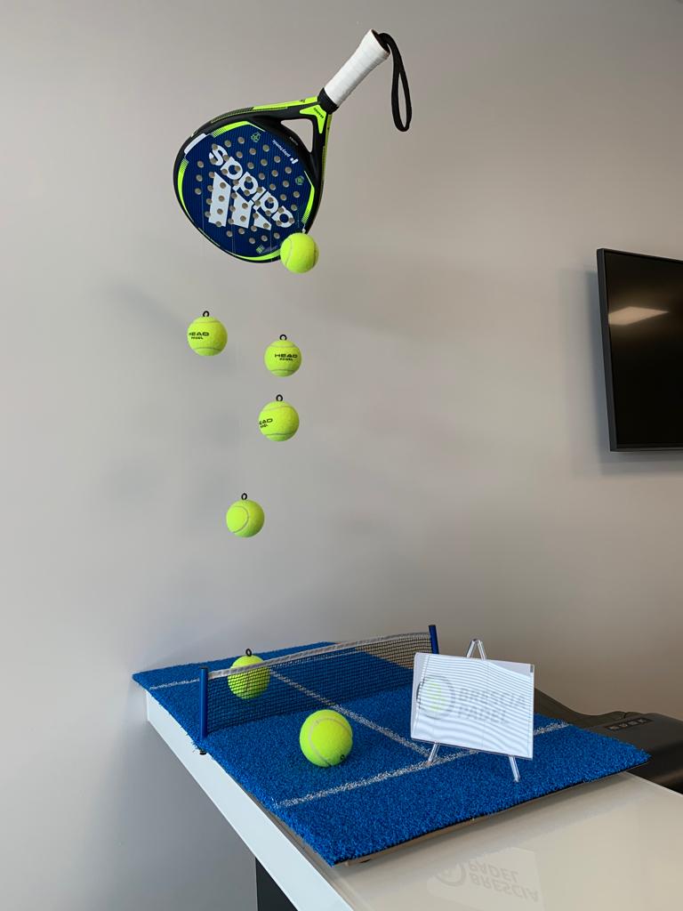 Racchetta da paddle con numerose palline da tennis gialle che fluttuano sopra un campo in miniatura, al chiuso.