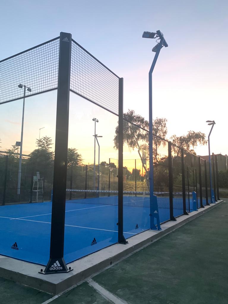 Campo da padel blu con rete nera e luci al tramonto.