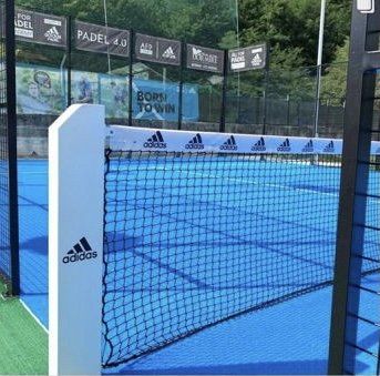 Campo da padel con marchio Adidas su rete e pali; campo blu, rete nera e striscioni degli sponsor.