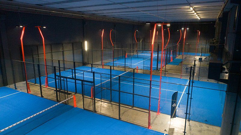 Campi da padel tennis al coperto con superfici blu, reti nere e illuminazione rossa.