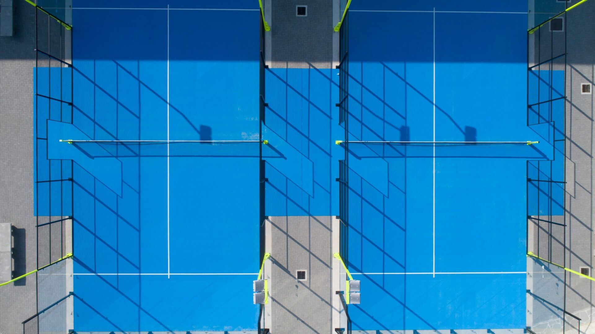 Vista dall'alto di due campi da padel blu con linee bianche e recinzione nera.