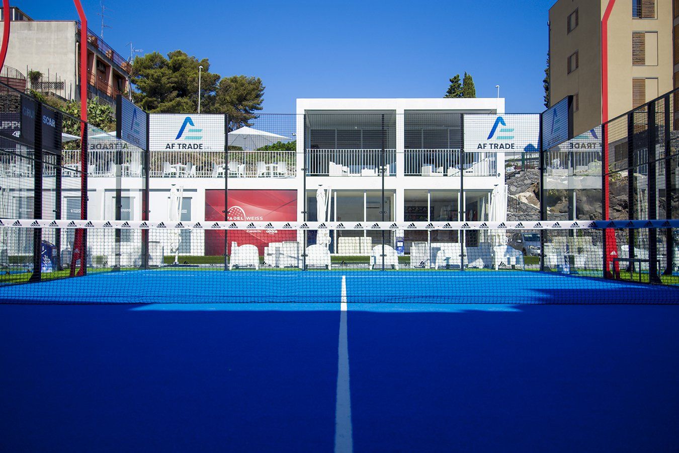 Campo da padel blu con rete, edificio bianco sullo sfondo sotto un cielo limpido.