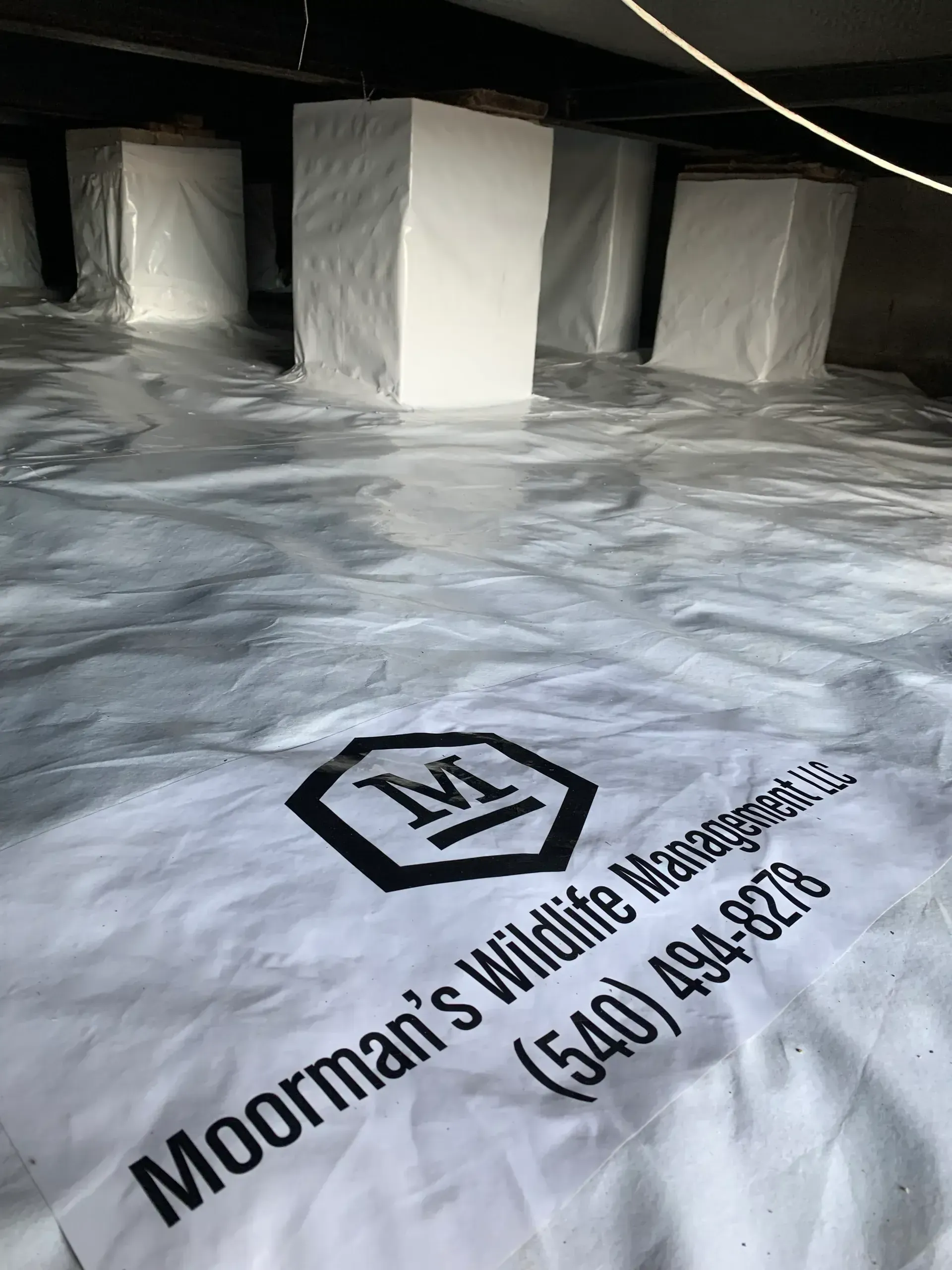 White crawlspace vapor barrier with support posts. Company logo and phone number printed.