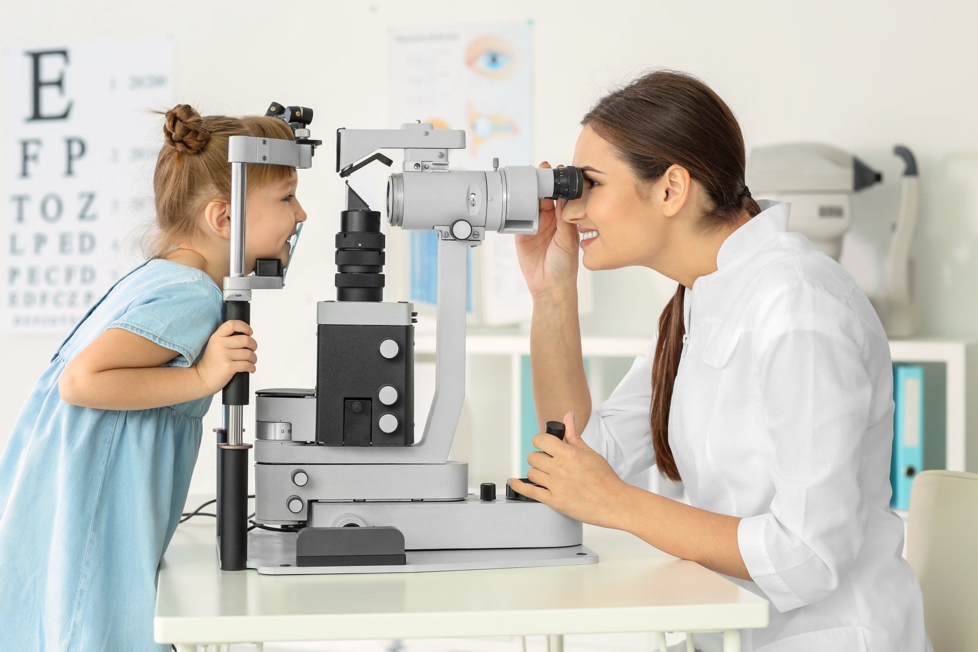 Eye doctor examining a young patient's eyes with a slit lamp in a clinic.