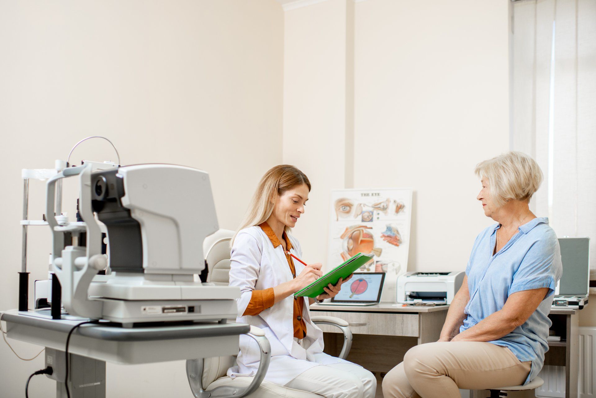 Optometrist consulting with a patient in an examination room, writing notes with an eye exam machine on the side.