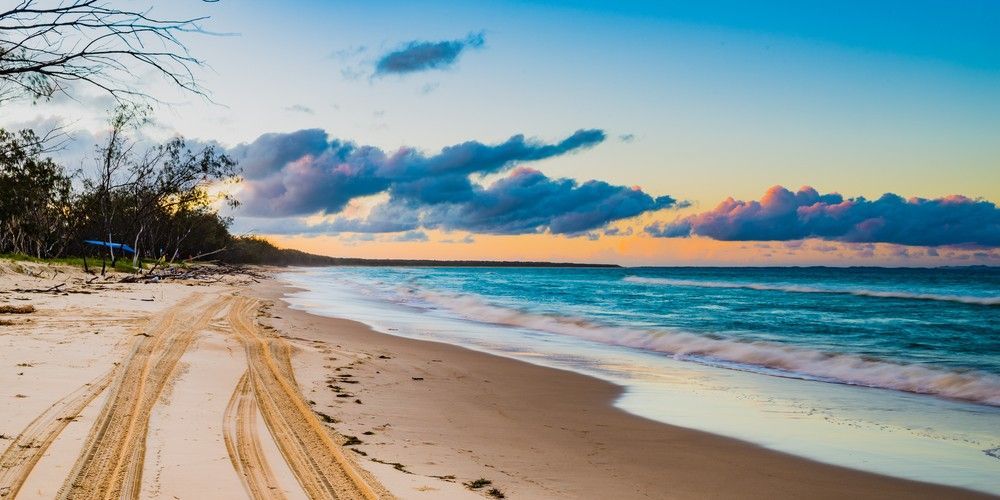 A Sandy Beach With Tire Tracks Leading to the Ocean at Sunset — Elite Stone in Byron Bay, NSW