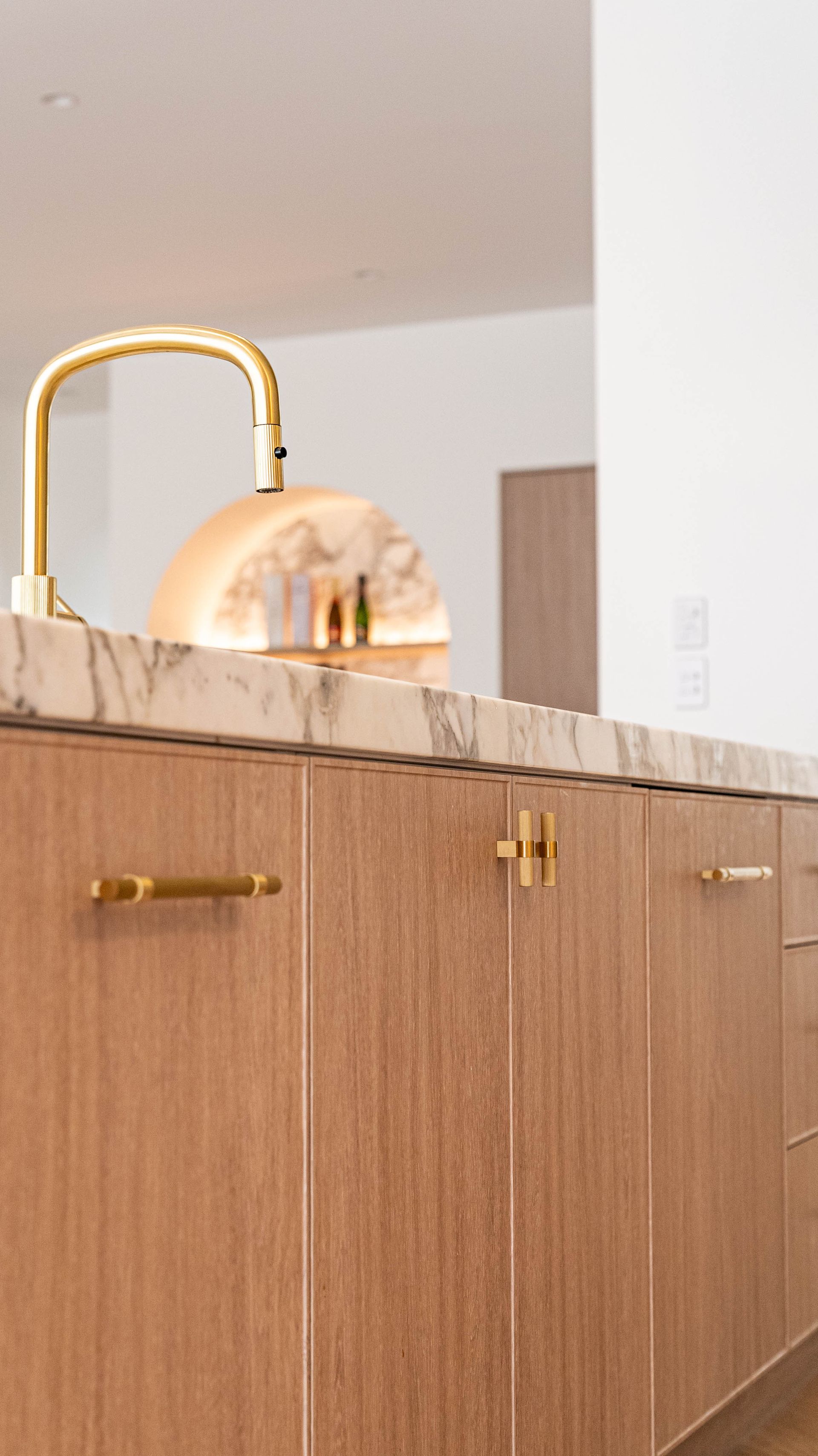 A kitchen island with wood-grain cabinets and gold hardware sits beneath a marble countertop with a gold faucet.
