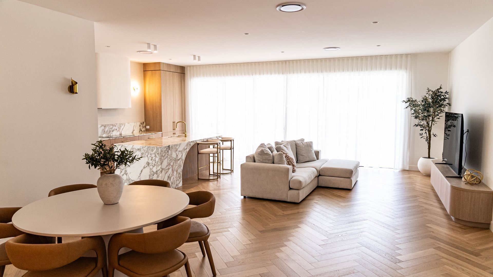 Open-plan living and dining area featuring a marble stone benchtop on the Gold Coast with herringbone timber floors and floor-to-ceiling sheer curtains