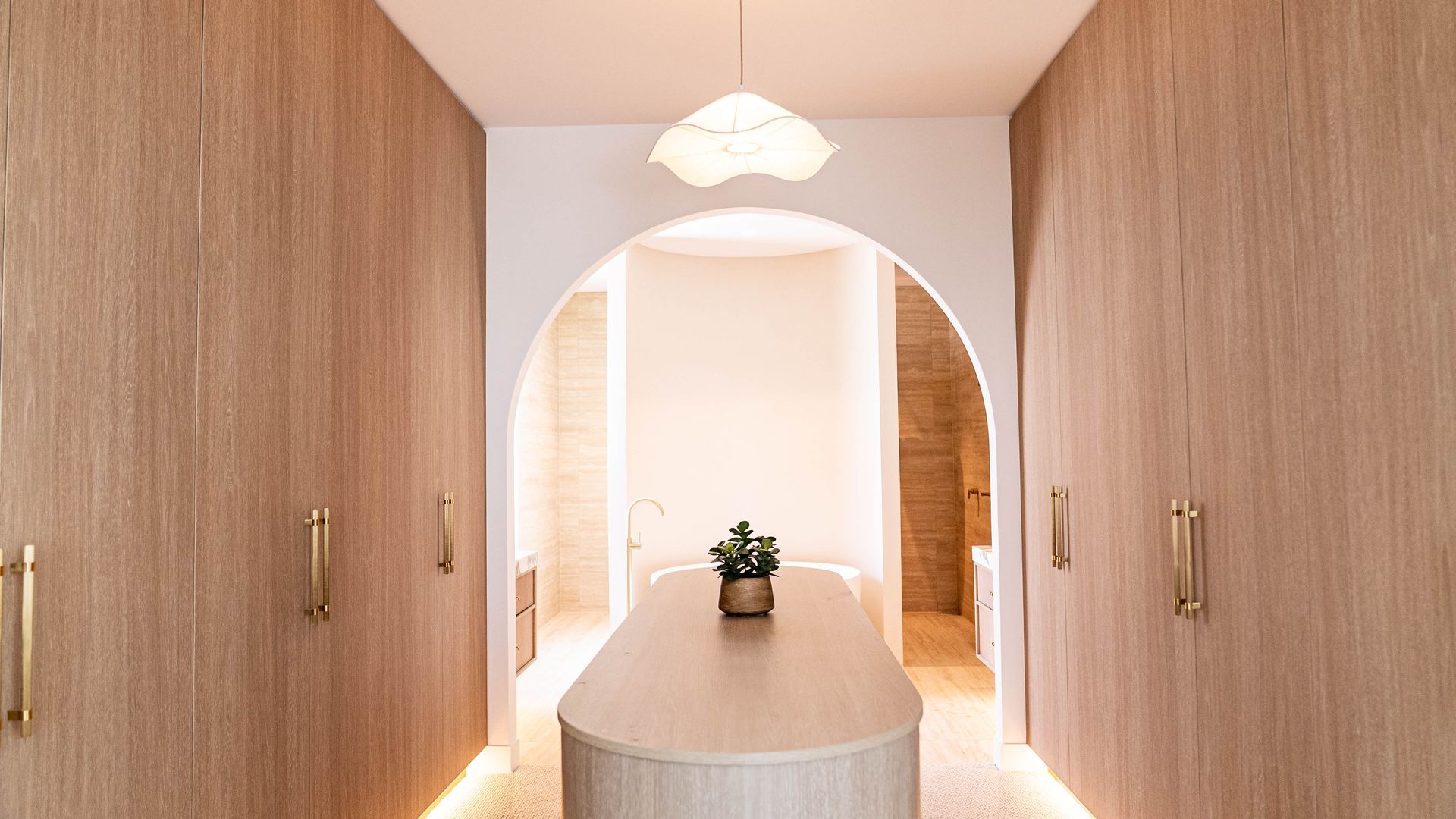 Modern hallway with wood-paneled walls, arched doorway, and a round table with a plant under pendant lighting
