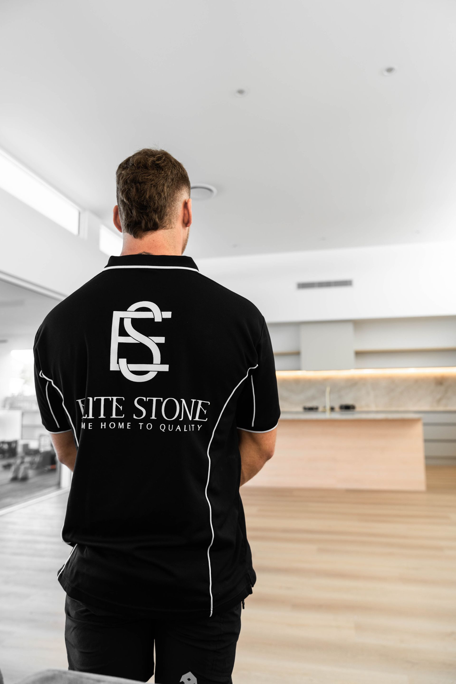 Elite Stone tradesperson in branded uniform standing in a completed kitchen, representing a trusted Gold Coast stone benchtop specialist